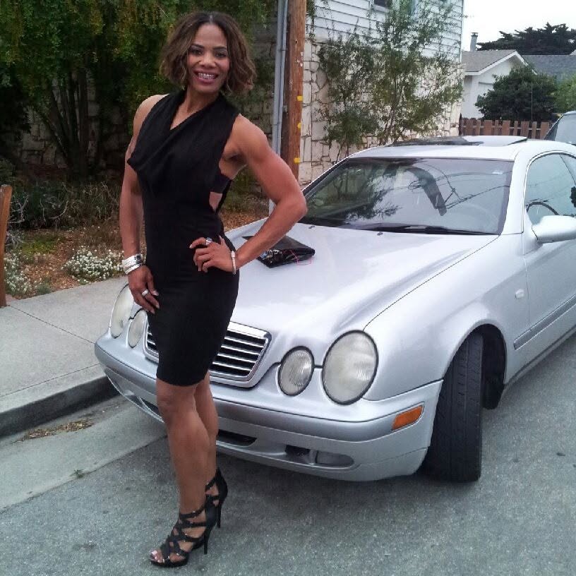 Chilone in a black evening dress posing confidently beside a silver car