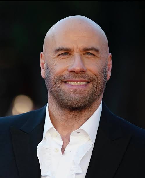 Red-carpet photo of a man with a salt-and-pepper beard smiling at the camera