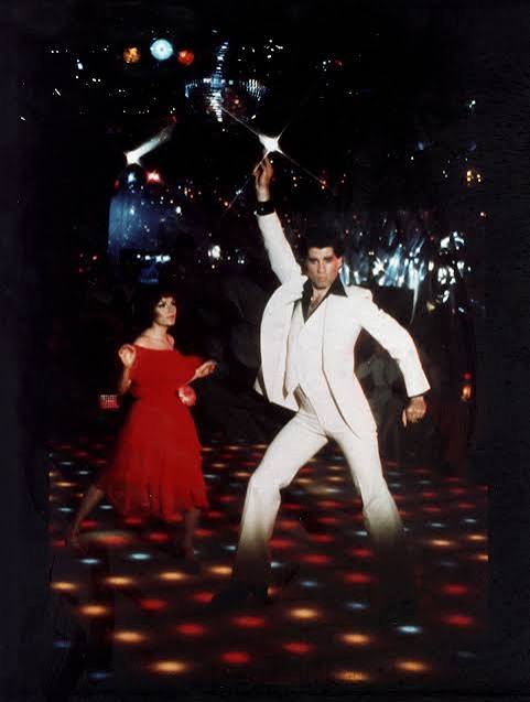 Still from Saturday Night Fever: a man dancing on an illuminated floor with one arm raised