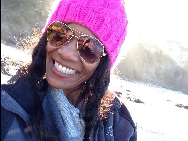 Chilone in a pink beanie and gold sunglasses at the beach, laughing