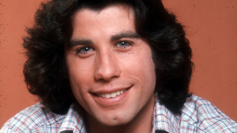 Studio headshot of a young man in a plaid shirt leaning forward and smiling